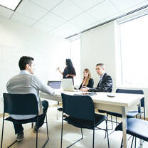 Three postgraduate students sit at a meeting room table while another writes on a whiteboard wall