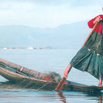Thai fisherman on traditional boat finishing with a net