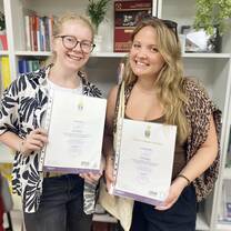 Two women hold their teaching certificates