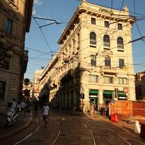 Historic street in Milan at golden hour featuring classic European architecture, tram tracks, and pedestrians exploring the city.