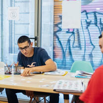 Students sitting around a table in a classroom, studying Spanish together with books and learning materials in a bright, modern setting.